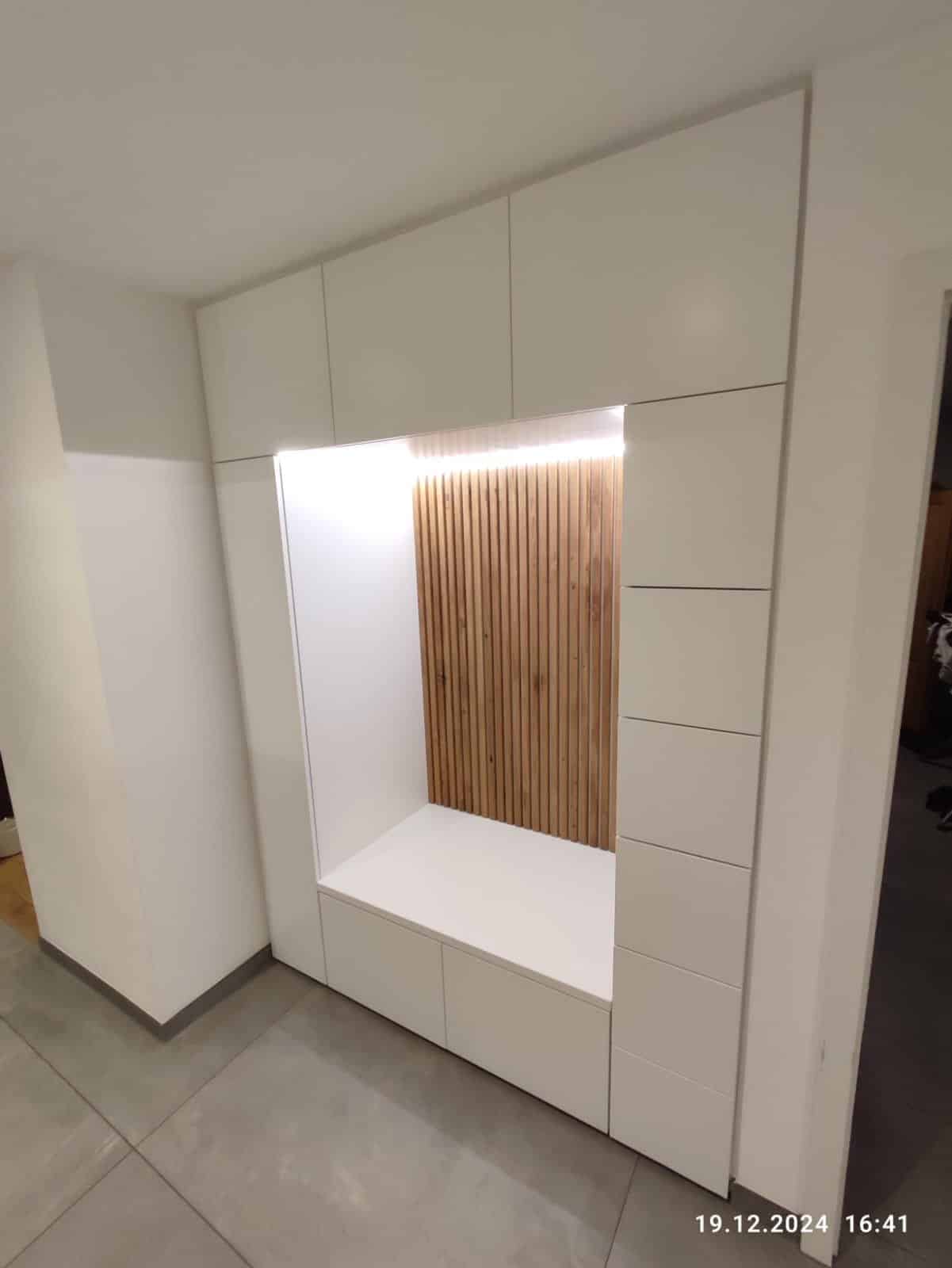 Weiße Garderobe mit geschlossenen Fronten und beleuchteter Sitznische vor senkrechten Holzleisten