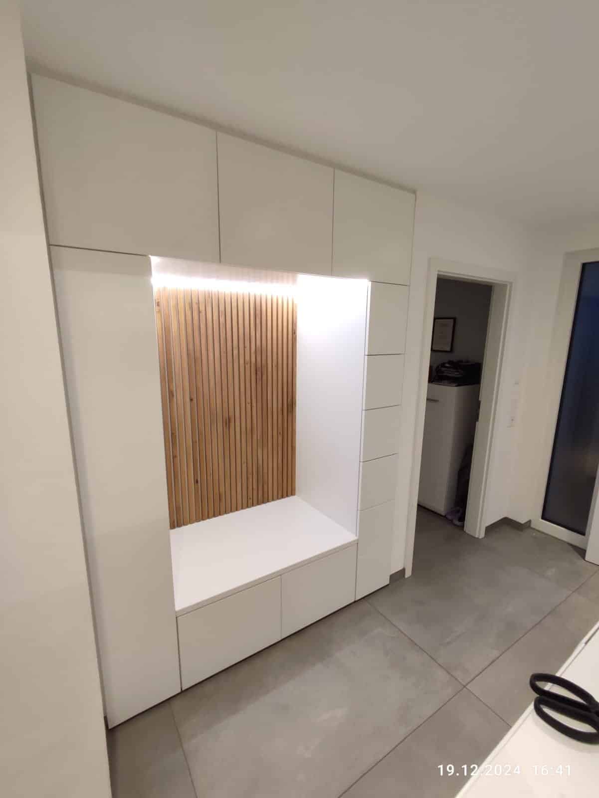 Gesamtansicht der weißen Garderobe im Flur mit Lichtnische und Stauraum bis zur Decke