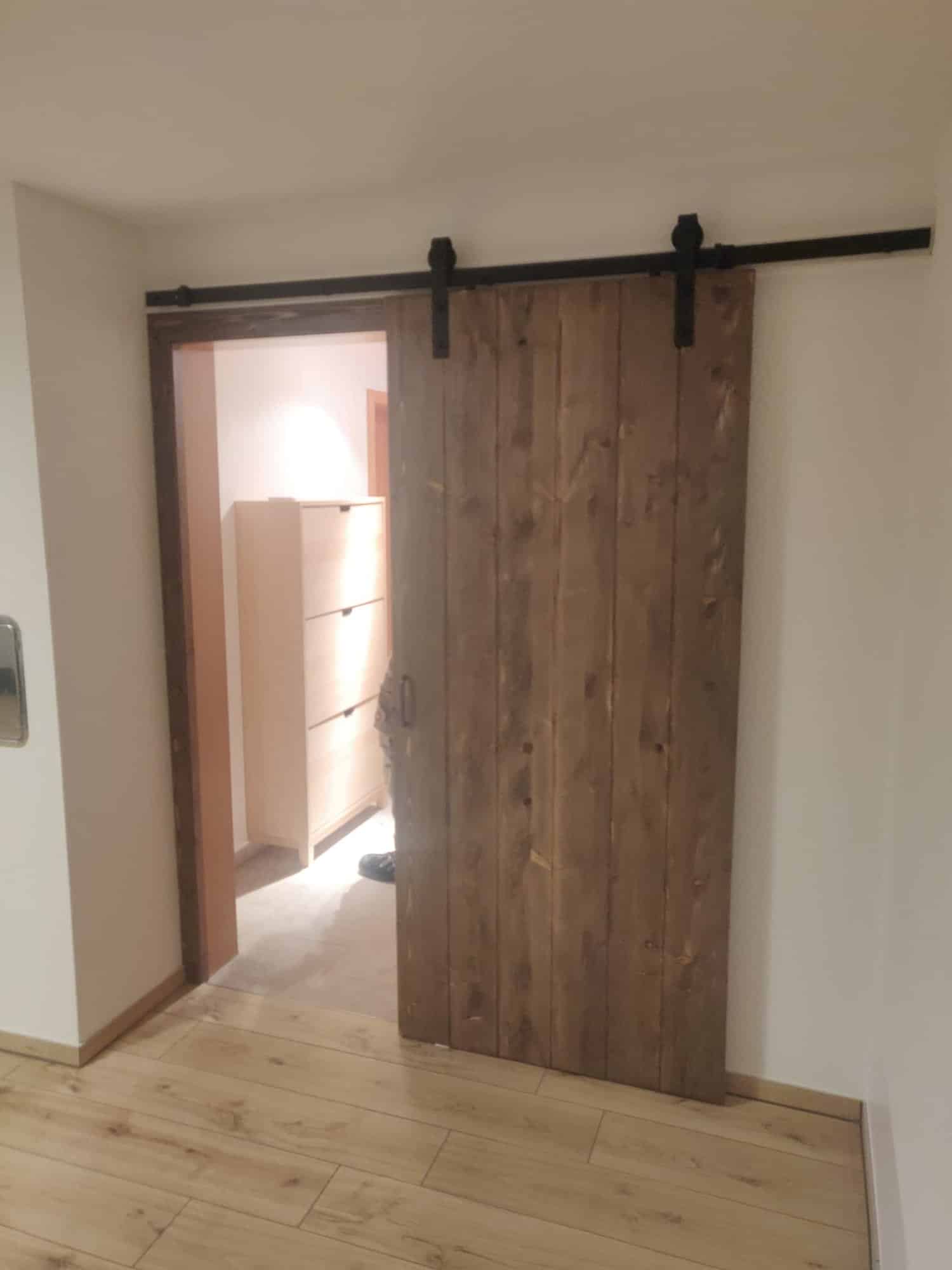 Seitlich geöffnete Holzschiebetür mit sichtbarer schwarzer Laufschiene