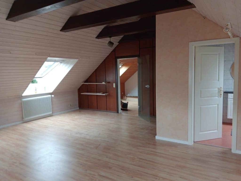 Heller Dachraum mit Holzfußboden, Dachfenstern und dunklen Balken