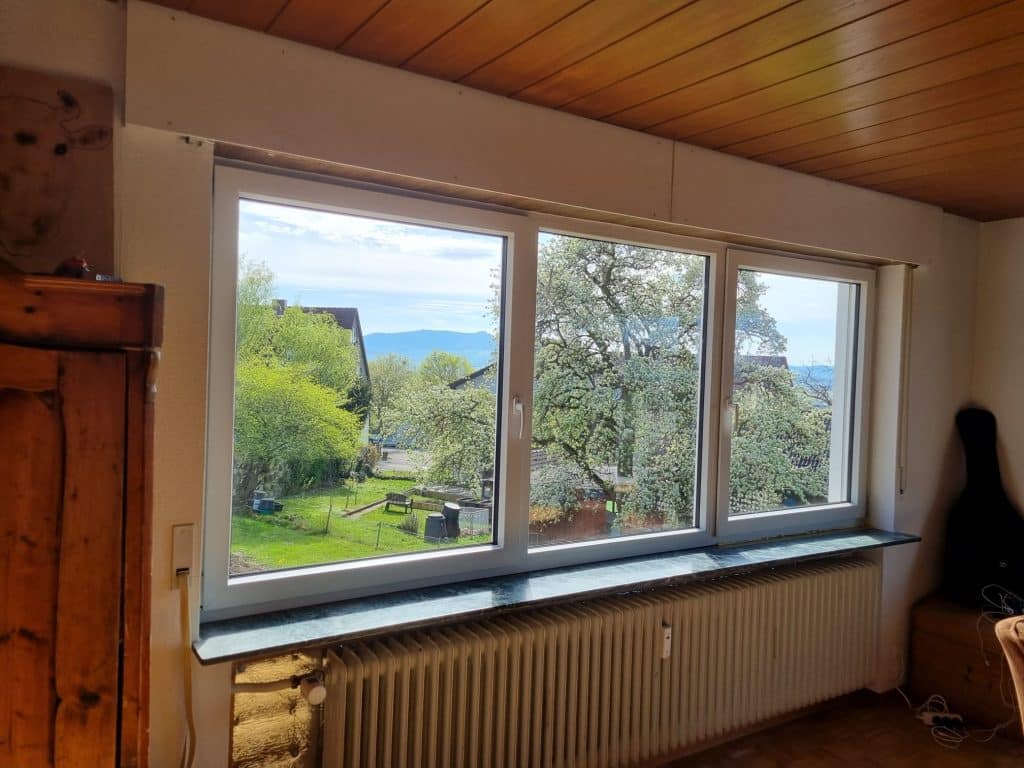 Breites weißes Fenster mit Blick in einen grünen Garten