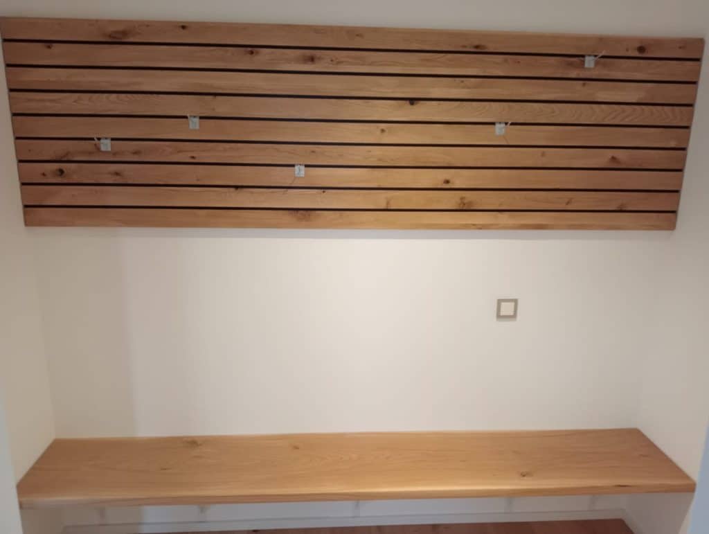 Sitzbank unter einer Garderobenwand aus horizontalen Holzlamellen