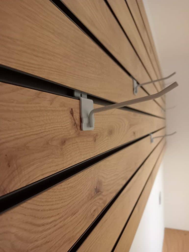 Nahaufnahme einer Garderobenwand aus Holzlamellen mit Metallhaken