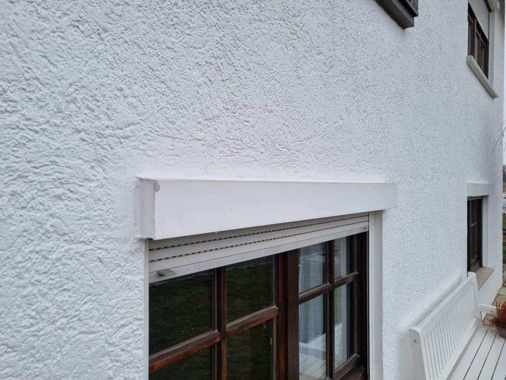 Weißer Rollladenkasten über einem dunklen Holzfenster an einer verputzten Hauswand